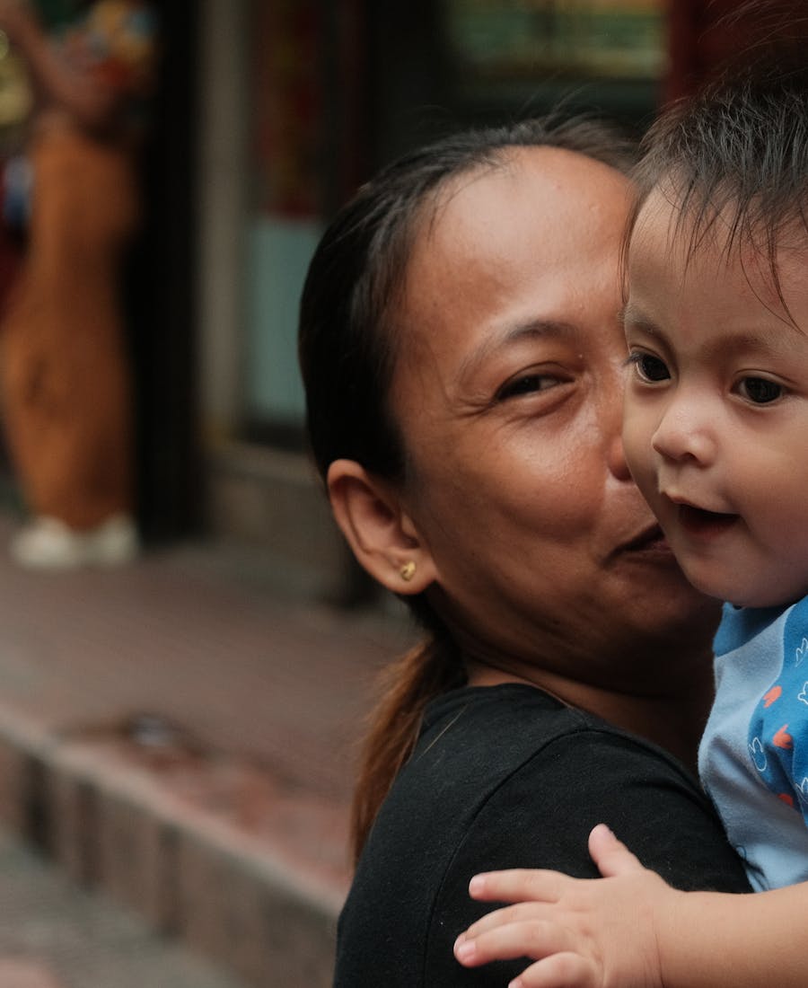 A mother carrying her child along a Manila street, gentle morning light.