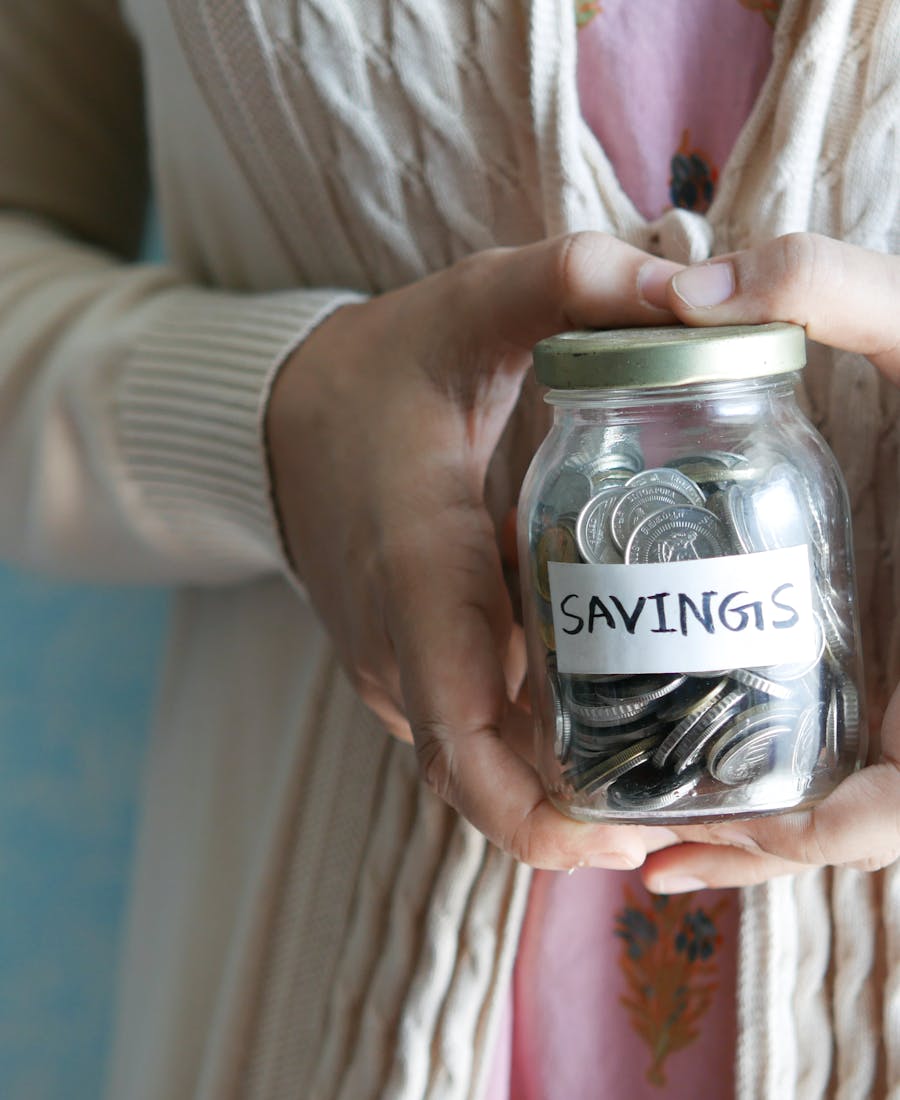 Hands gently placing coins into a savings jar in warm afternoon light.